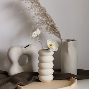 Three ceramic vases with flowers and dried plants on a neutral background
