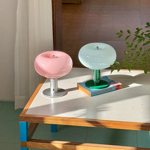 Two small decorative lamps on a wooden table with a plant in the background.