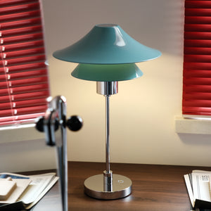 Table lamp with a green shade on a desk in a room with red blinds.