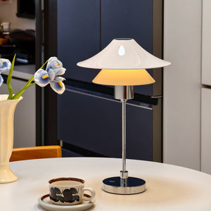 Table lamp on a table with a vase of flowers and a cup in the background.