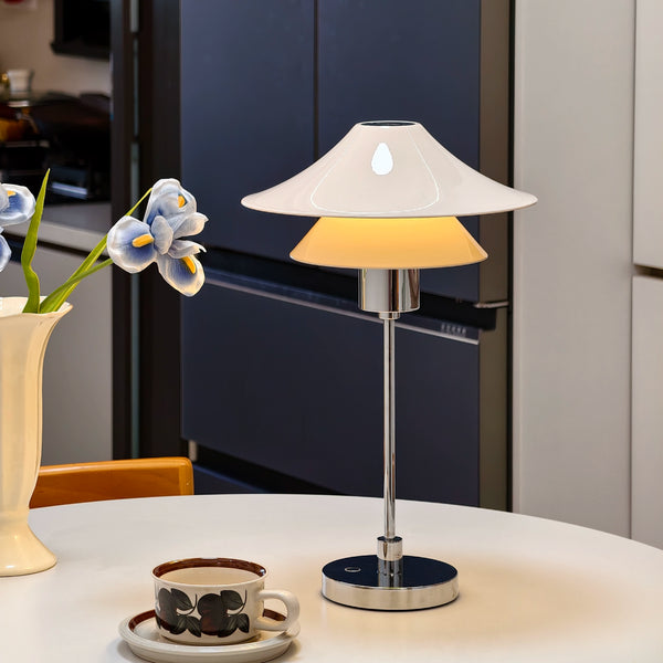 Table lamp on a table with a vase of flowers and a cup in the background.