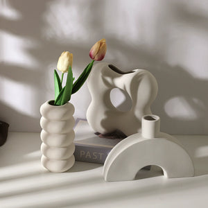 Three white ceramic vases with different shapes on a light surface with a blurred background