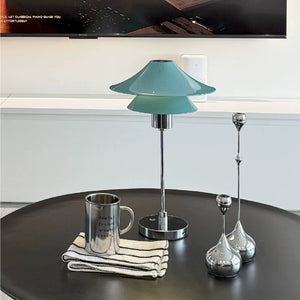 Teal table lamp on a round black surface with a TV in the background
