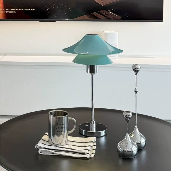 Teal table lamp on a round black surface with a TV in the background