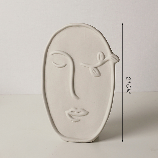 Ceramic wall art in the shape of a face with measurements on a plain background